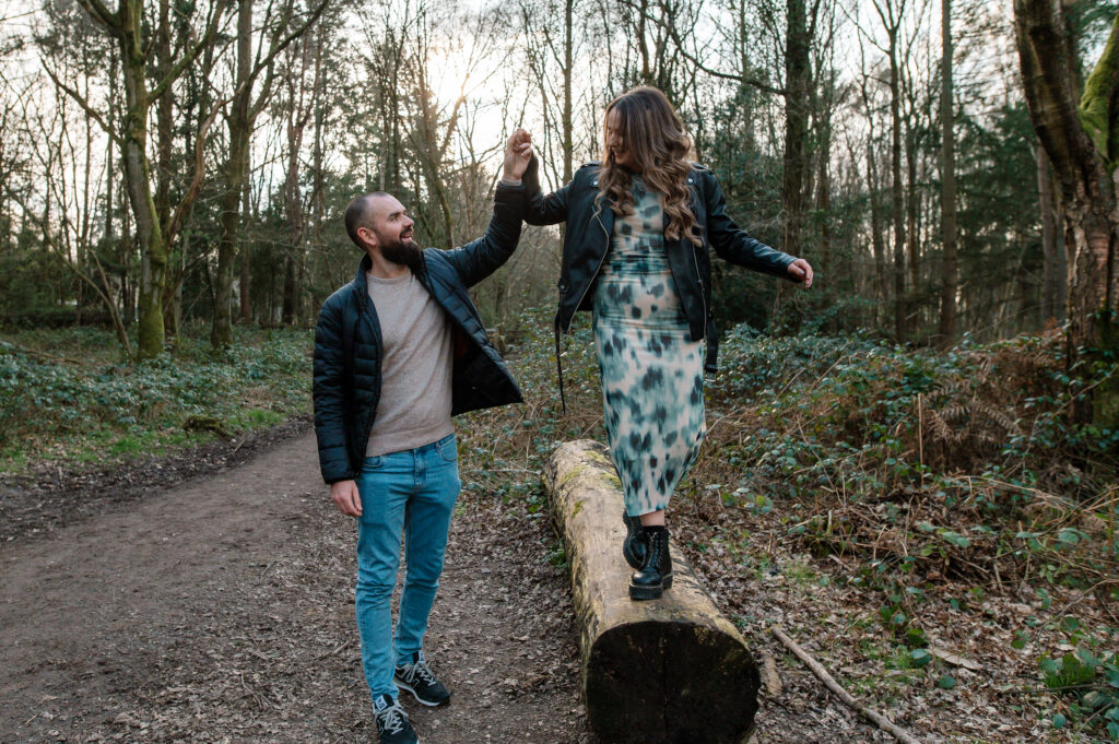 Tom holds Chelsey's hand and guides her whilst she walks across a wooden log in oakley woods