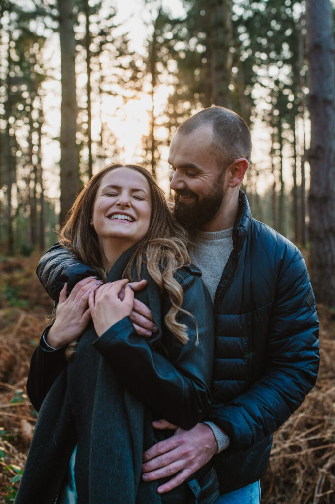 Tom stands behind Chelsey and cuddles her as Chelsey smiles in oakley woods