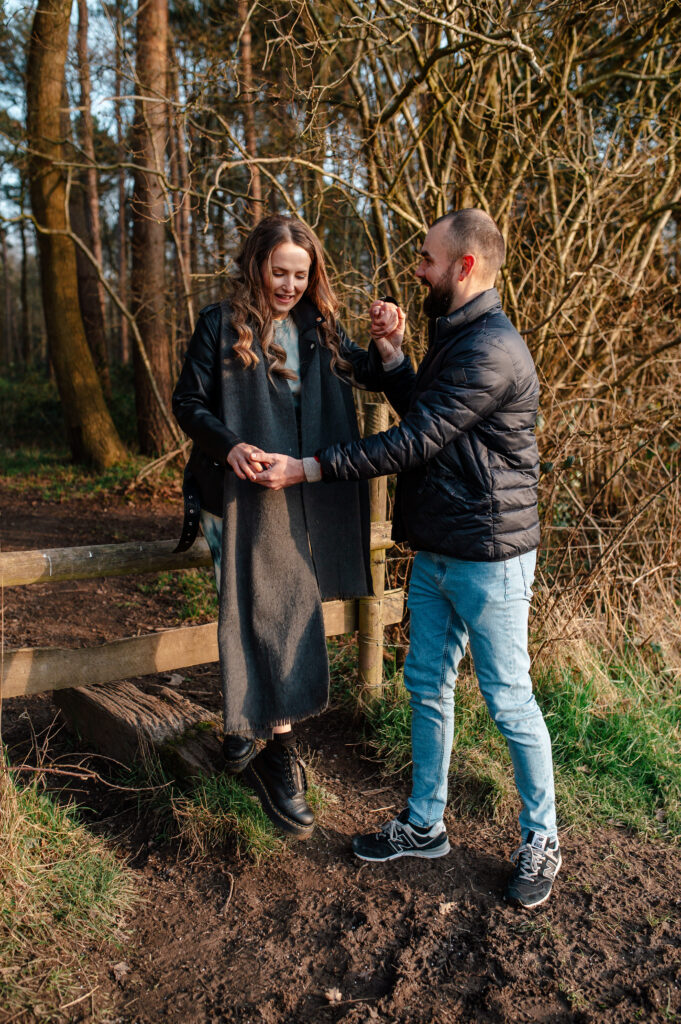 Tom helps Chelsey over the wooden sty holding both of her hands as she steps down into the surrounding fields in oakley woods