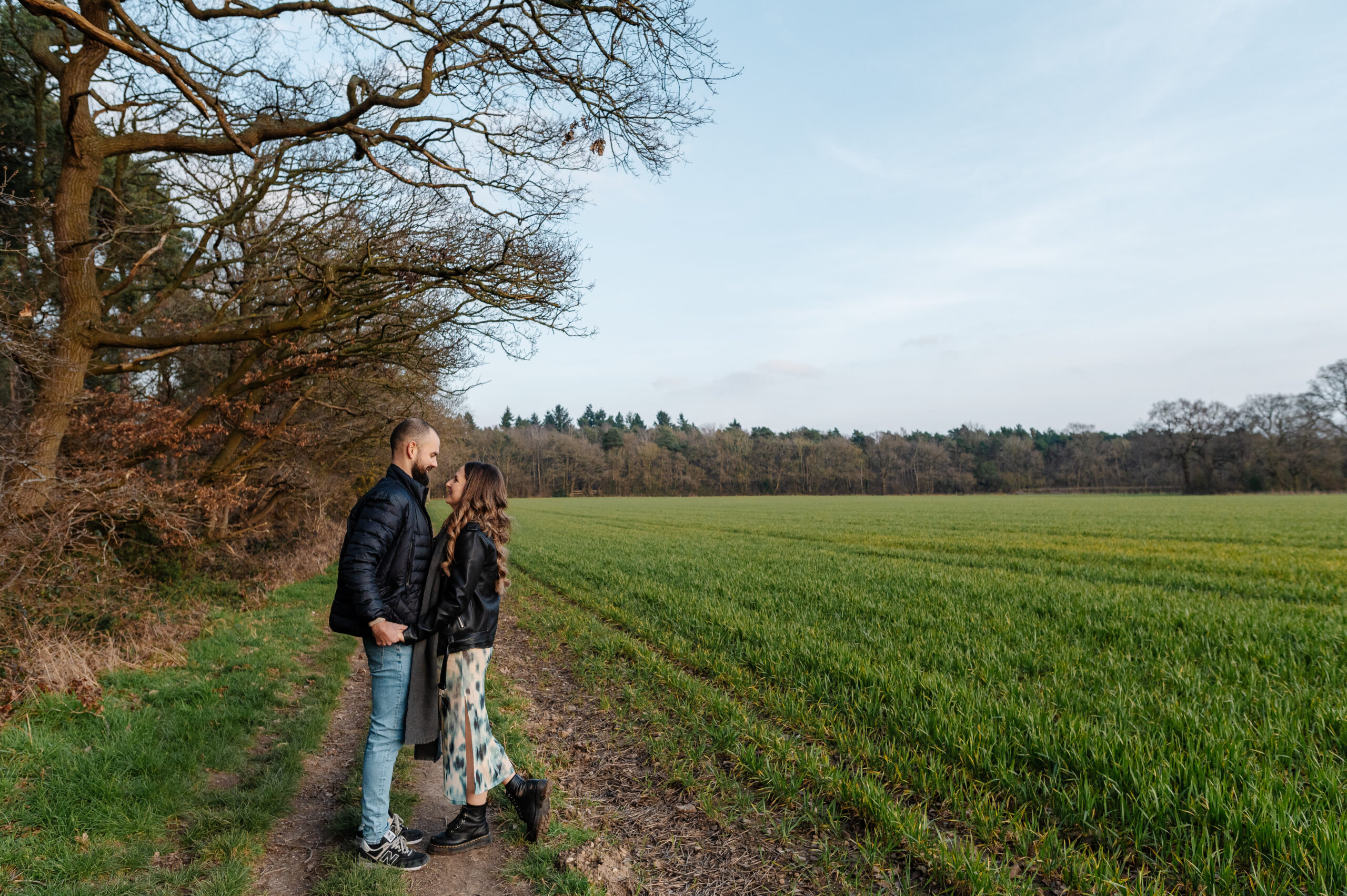 Pre-wedding shoot at Oakley woods in Warwickshire. Couple holding hands in the field next to the forest