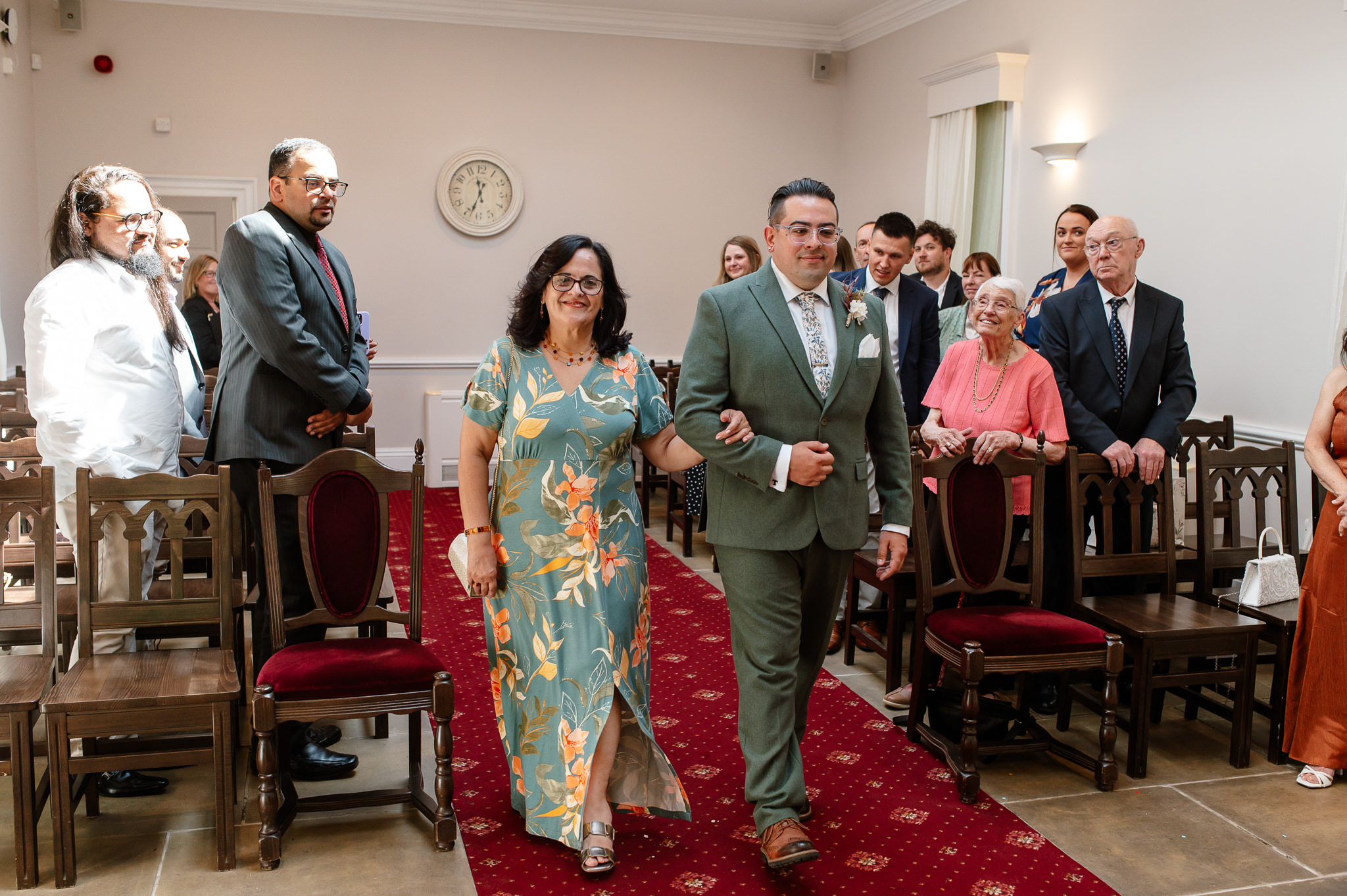 groom walking up the aisle with his mum in york registry office during wedding  
