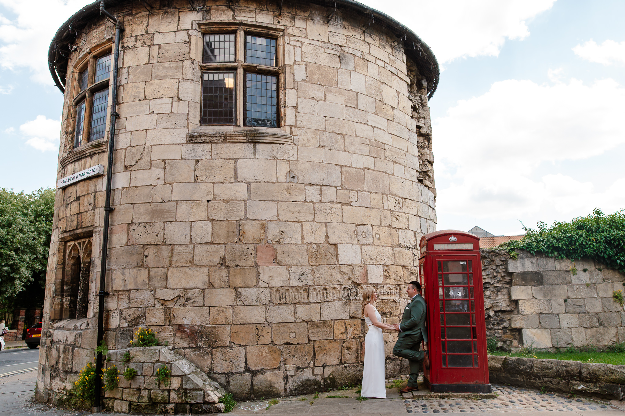 Groom leaning against telephone box facing bride holding hands at the top of Marygate in York after York registry office wedding ceremony