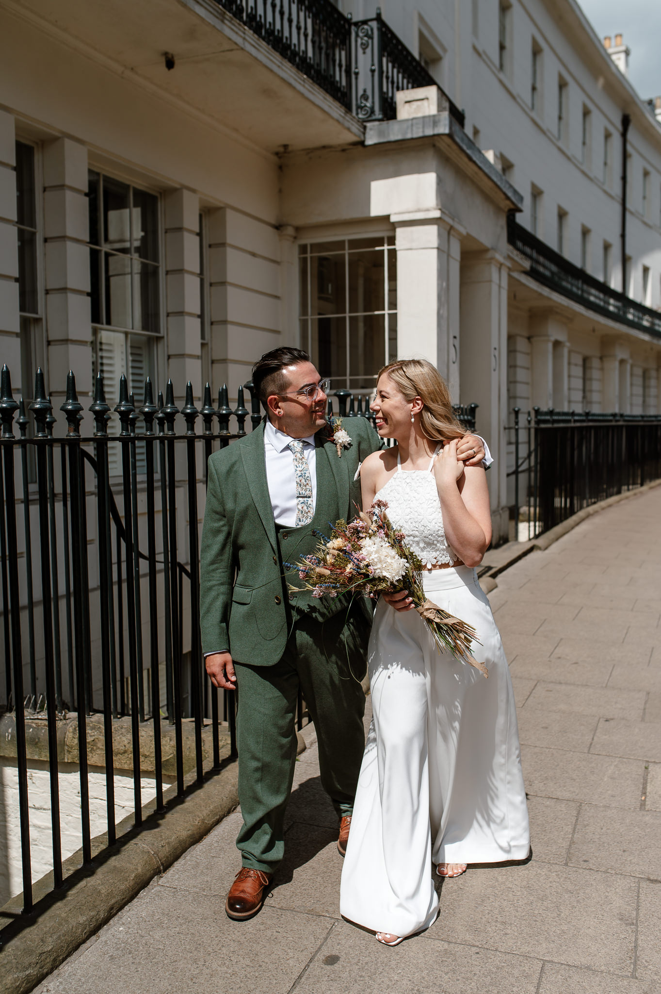 groom with his arm over brides shoulder looking at each other smiling 
