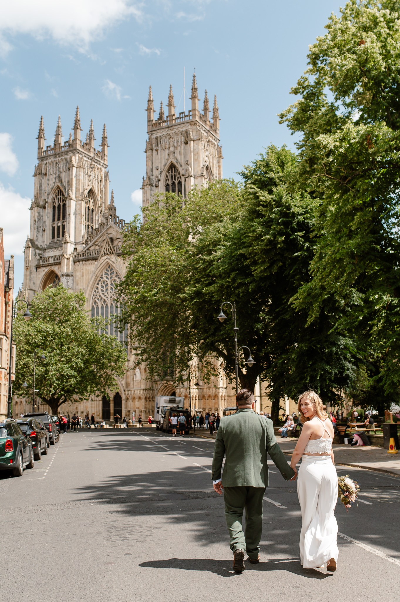 bride and groom walking away and bride looking back whilst walking towards york minster
