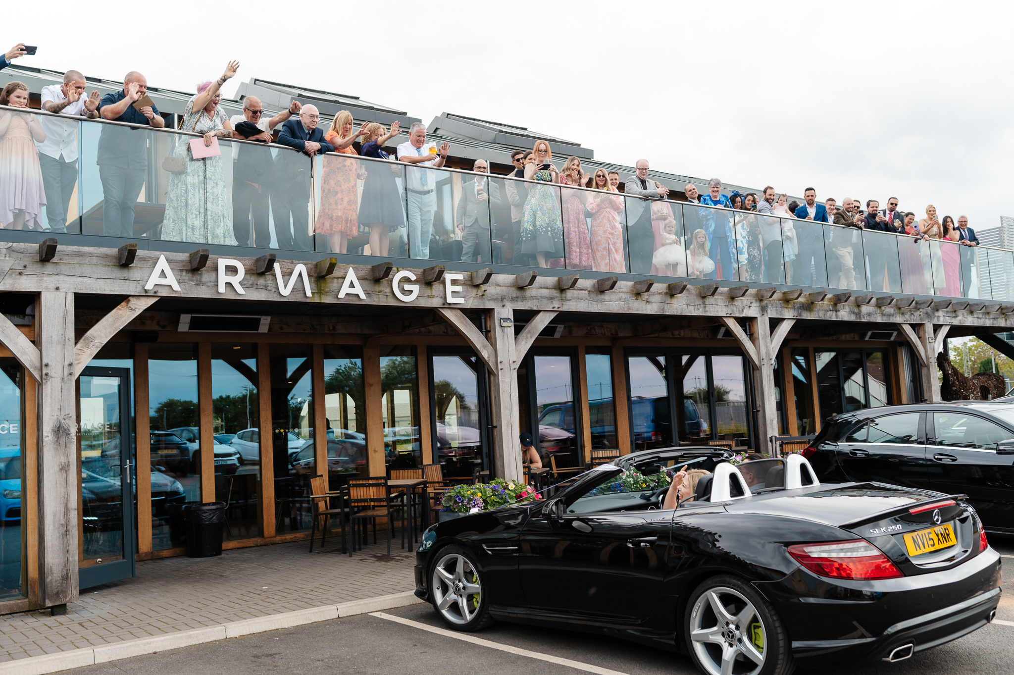 bride and groom arriving in brides convertible car whilst guests wave and welcome them from the balcony
